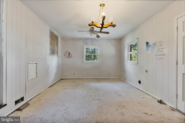 carpeted spare room with wooden walls and ceiling fan with notable chandelier