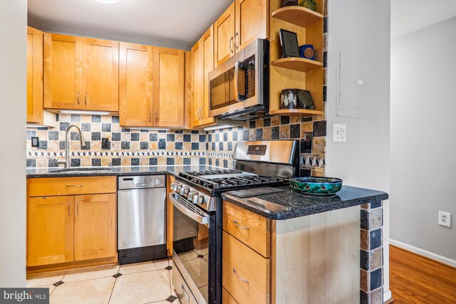 kitchen with sink, tasteful backsplash, dark stone countertops, light hardwood / wood-style floors, and appliances with stainless steel finishes