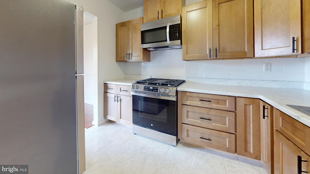 kitchen with appliances with stainless steel finishes, light tile patterned floors, and decorative backsplash