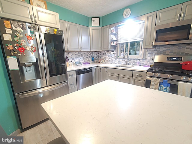 kitchen with decorative backsplash, sink, appliances with stainless steel finishes, gray cabinets, and a textured ceiling