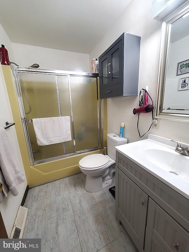 full bathroom featuring wood-type flooring, shower / bath combination with glass door, vanity, and toilet