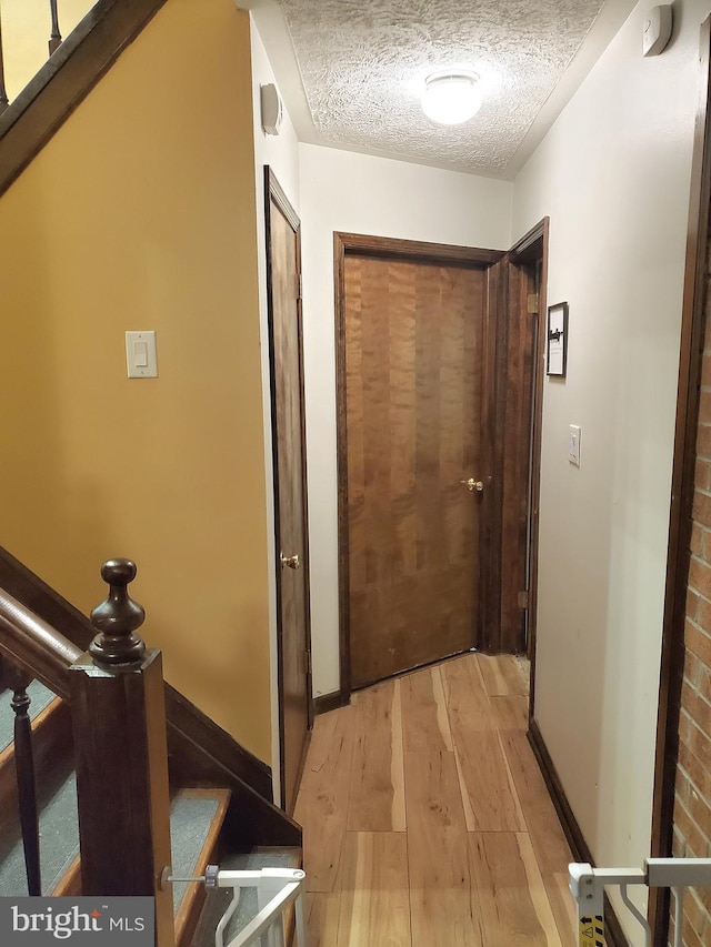 hall with a textured ceiling and light wood-type flooring