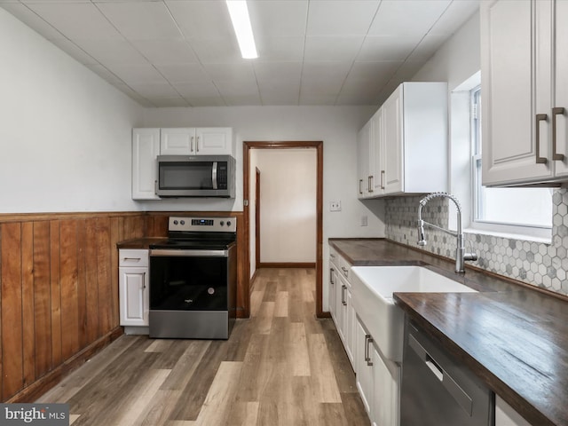 kitchen featuring wood-type flooring, backsplash, wood counters, stainless steel appliances, and white cabinets