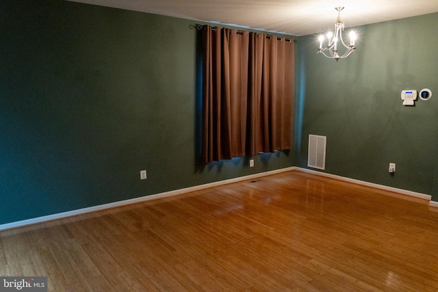 spare room featuring an inviting chandelier, visible vents, baseboards, and wood finished floors