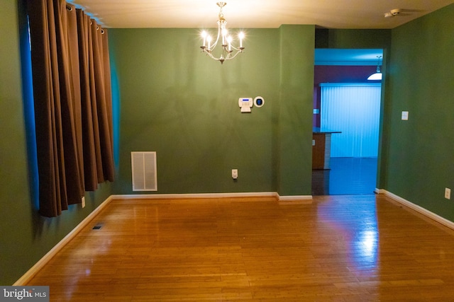 empty room featuring a chandelier, visible vents, baseboards, and wood finished floors