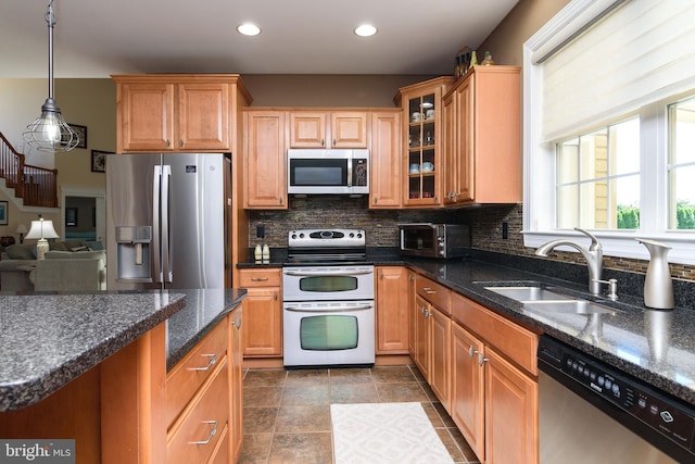 kitchen featuring decorative backsplash, stainless steel appliances, sink, dark stone counters, and decorative light fixtures