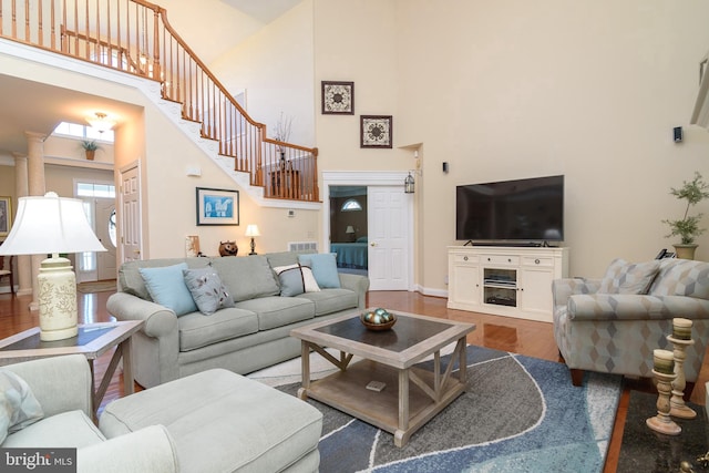 living room featuring a towering ceiling, a fireplace, dark wood-type flooring, and decorative columns