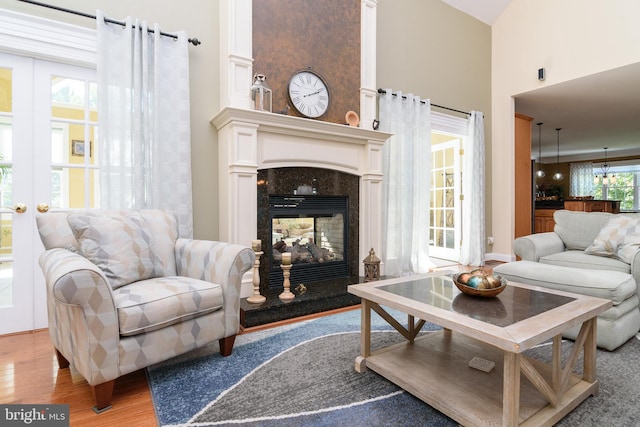 living room with french doors, light hardwood / wood-style flooring, a premium fireplace, and a high ceiling