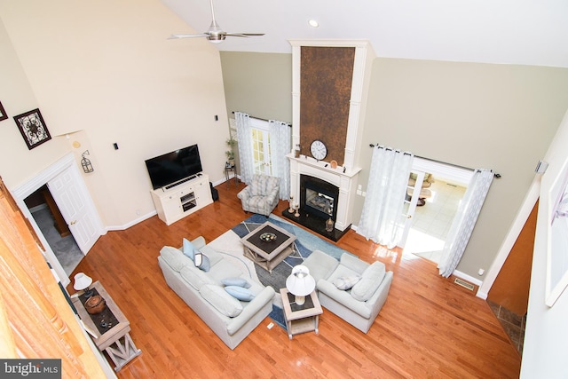 living room with ceiling fan, hardwood / wood-style floors, high vaulted ceiling, and a large fireplace