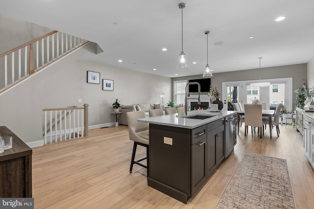 kitchen featuring a kitchen breakfast bar, an island with sink, dishwasher, light hardwood / wood-style flooring, and decorative light fixtures