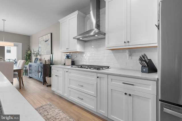 kitchen with appliances with stainless steel finishes, white cabinetry, pendant lighting, light hardwood / wood-style flooring, and wall chimney range hood