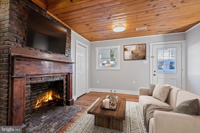 living room featuring a brick fireplace, wood-type flooring, crown molding, and wooden ceiling