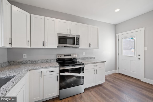 kitchen with appliances with stainless steel finishes, white cabinetry, hardwood / wood-style floors, and light stone counters