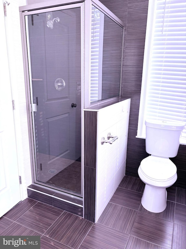 bathroom featuring tile patterned flooring, toilet, and an enclosed shower