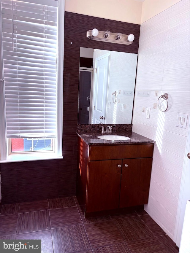 bathroom with tile walls, vanity, a shower with door, and tile patterned floors