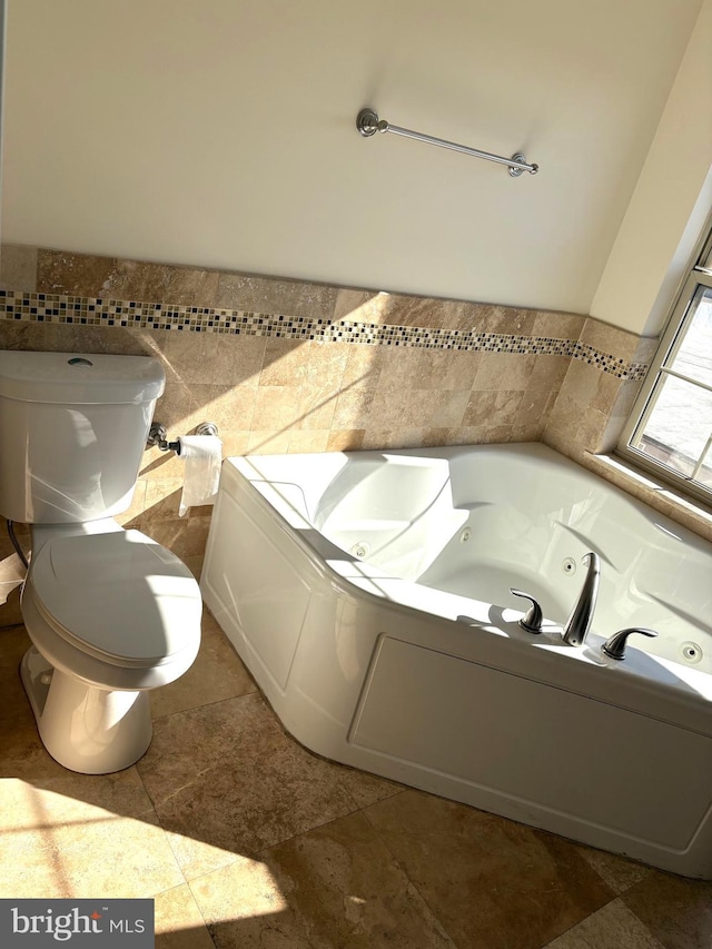 bathroom featuring toilet, a tub to relax in, and tile walls