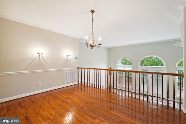 unfurnished room with wood-type flooring, a notable chandelier, and crown molding