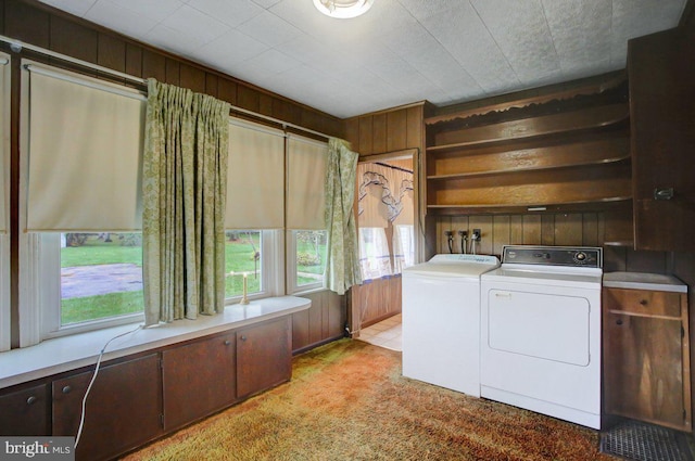 clothes washing area featuring light carpet, separate washer and dryer, and wooden walls