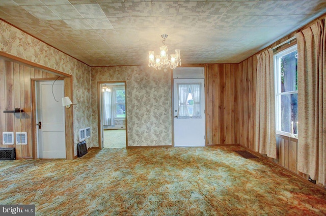 carpeted spare room with an inviting chandelier and wood walls