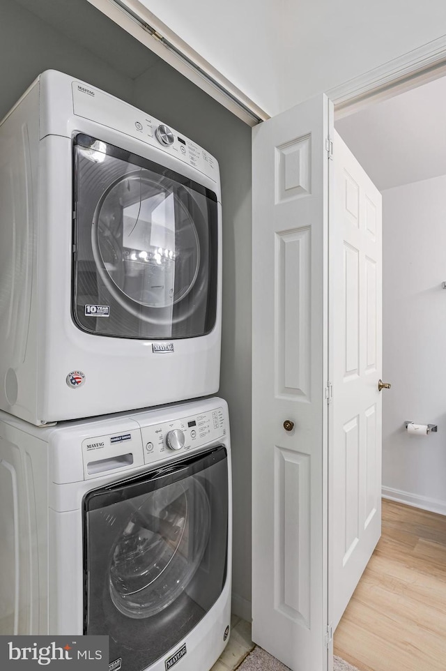 laundry room with light wood-type flooring and stacked washer and clothes dryer