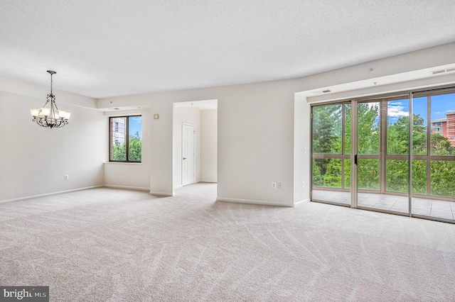 spare room featuring light colored carpet, a notable chandelier, and a textured ceiling