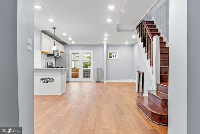 interior space with white cabinets, radiator, pendant lighting, backsplash, and light wood-type flooring