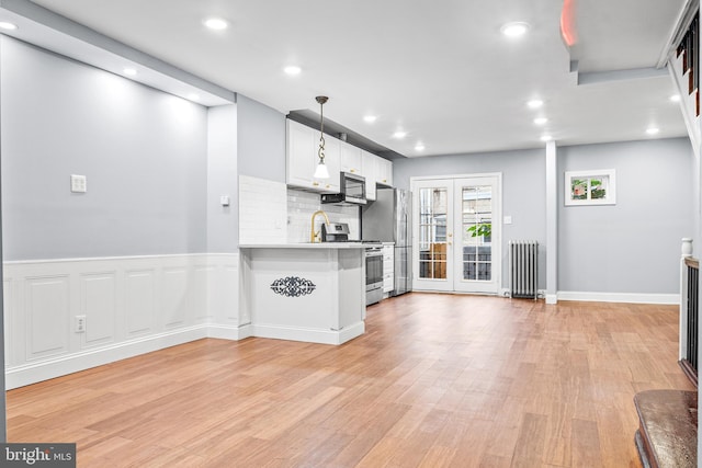 kitchen with radiator, pendant lighting, white cabinetry, appliances with stainless steel finishes, and light wood-type flooring