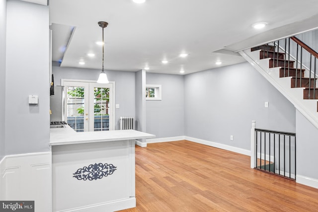 kitchen featuring light hardwood / wood-style floors, kitchen peninsula, hanging light fixtures, radiator, and french doors