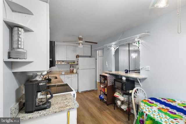 kitchen featuring light hardwood / wood-style floors, white refrigerator, white cabinets, black range oven, and ceiling fan