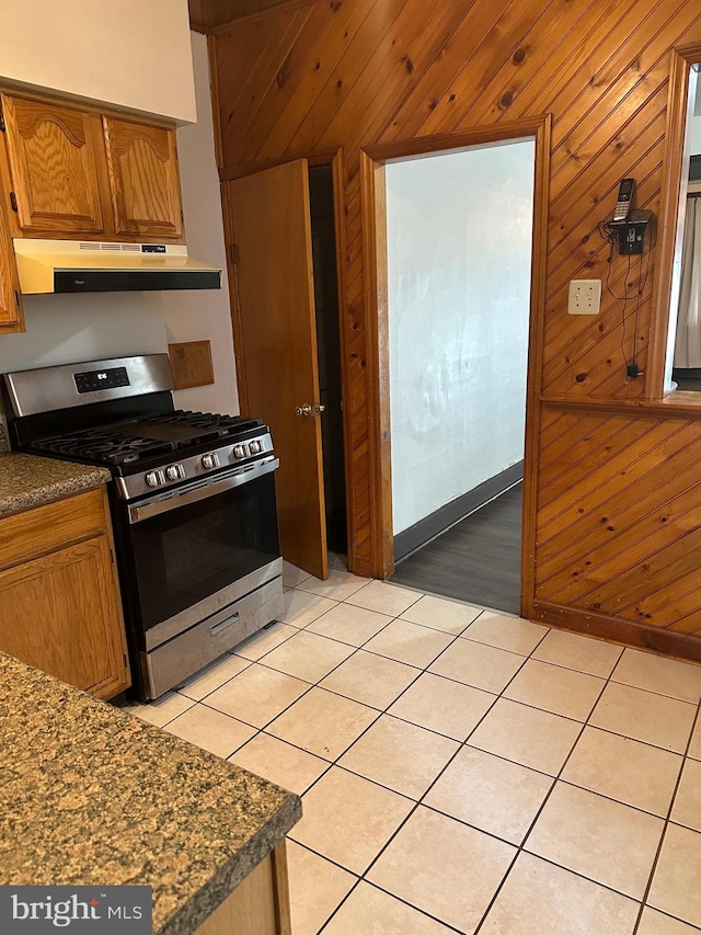 kitchen featuring wood walls, stainless steel range with gas stovetop, and light tile patterned floors