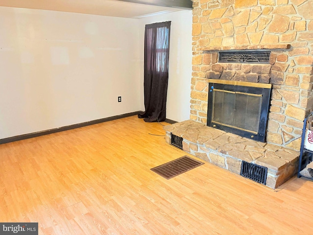 unfurnished living room with hardwood / wood-style flooring and a stone fireplace