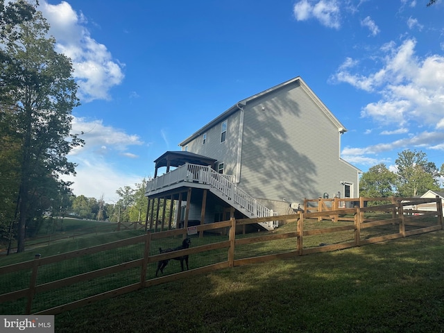 rear view of house with a wooden deck, a rural view, and a lawn