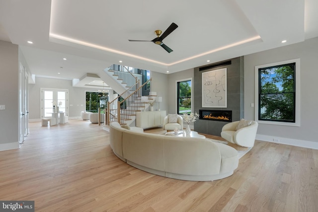 living room with a tile fireplace, light hardwood / wood-style flooring, a tray ceiling, and a healthy amount of sunlight