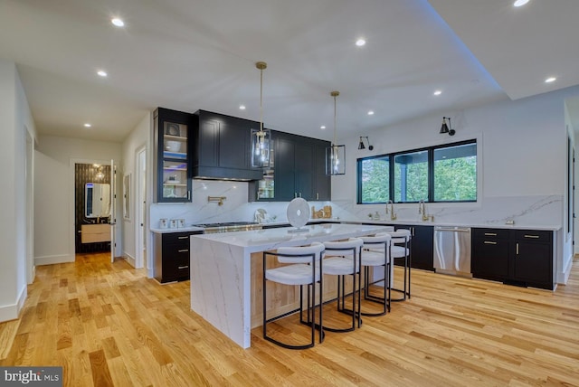 kitchen with light wood-type flooring, a kitchen island, stainless steel dishwasher, decorative light fixtures, and light stone countertops