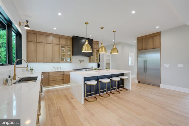 kitchen with custom exhaust hood, sink, stainless steel appliances, a spacious island, and light wood-type flooring