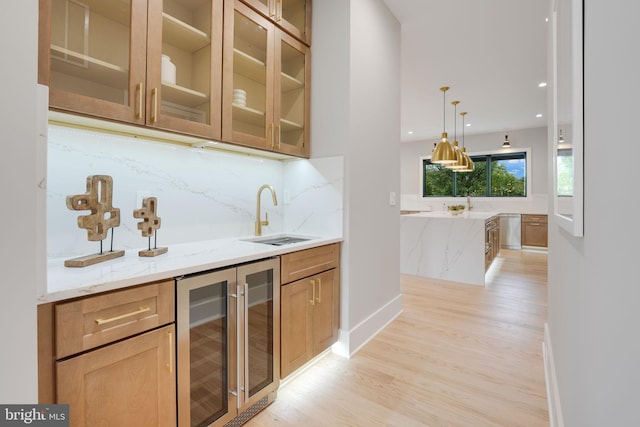 bar with wine cooler, sink, light hardwood / wood-style flooring, decorative light fixtures, and light stone countertops