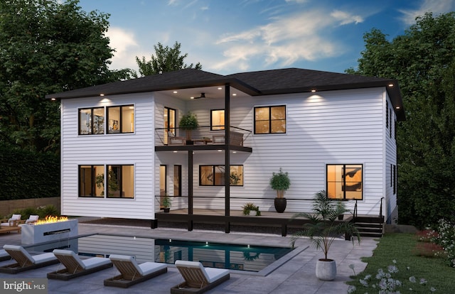 back house at dusk with a patio, a balcony, and an outdoor living space with a fire pit