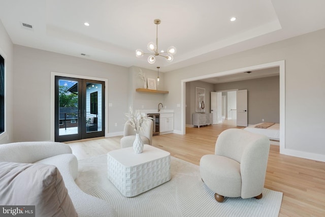 living room with wine cooler, light hardwood / wood-style flooring, french doors, and a notable chandelier