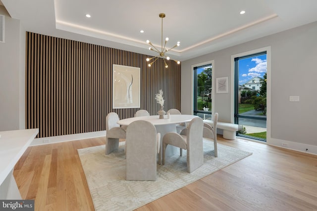 dining area featuring light hardwood / wood-style flooring, a notable chandelier, and a raised ceiling