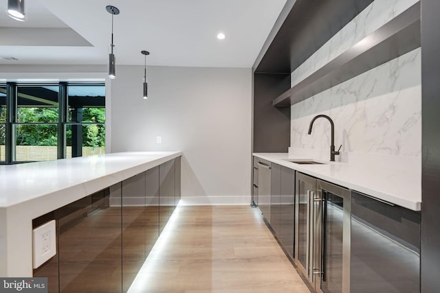 kitchen featuring pendant lighting, light wood-type flooring, tasteful backsplash, and sink