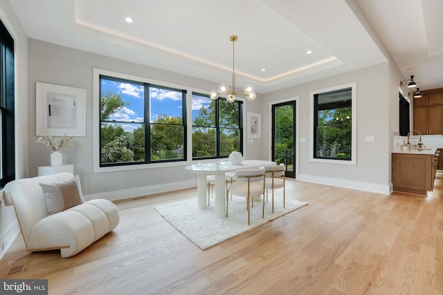 dining area with an inviting chandelier, light wood-type flooring, and a tray ceiling