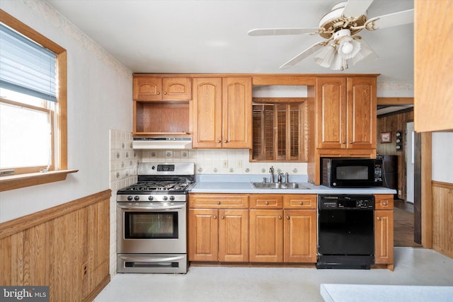 kitchen with wood walls, black appliances, sink, and ceiling fan