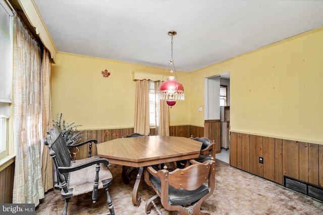 dining room with crown molding, wood walls, and light colored carpet