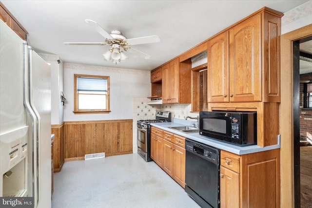 kitchen featuring wood walls, black appliances, sink, backsplash, and ceiling fan