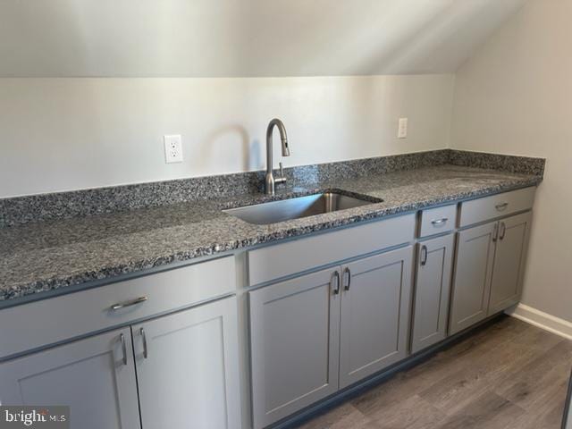 kitchen featuring dark wood-type flooring, dark stone countertops, sink, vaulted ceiling, and gray cabinets