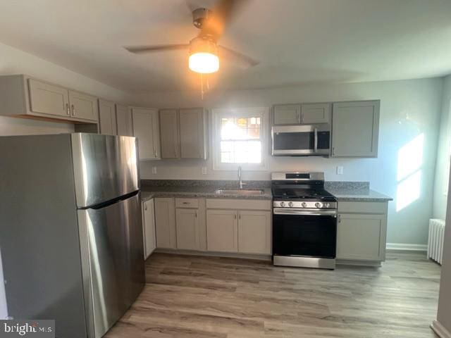 kitchen with radiator heating unit, hardwood / wood-style flooring, stainless steel appliances, and sink