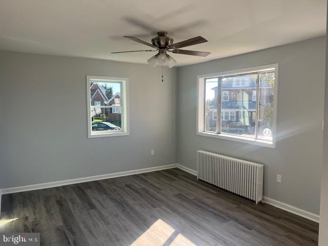 empty room with radiator, ceiling fan, a healthy amount of sunlight, and dark hardwood / wood-style flooring