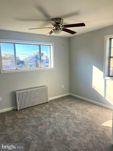 carpeted empty room with plenty of natural light, ceiling fan, and radiator