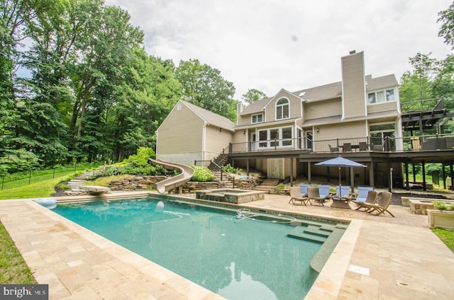 view of swimming pool with a water slide, a deck, a patio area, and an in ground hot tub