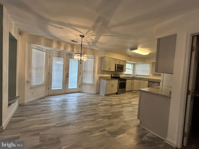 kitchen with appliances with stainless steel finishes, light stone counters, pendant lighting, an inviting chandelier, and french doors